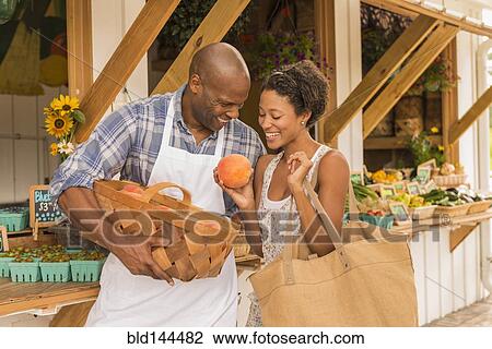 Stock Image - African American people examining produce at farmers market. Fotosearch