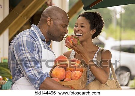 Stock Photograph - African American people smelling produce at farmers market. Fotosearch
