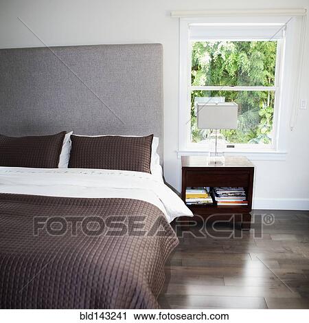 Stock Image - Bed, night table and window in modern bedroom. Fotosearch