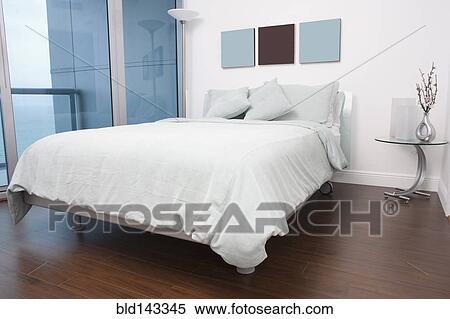 Stock Photography - Bed, wall art and night table in modern bedroom. Fotosearch