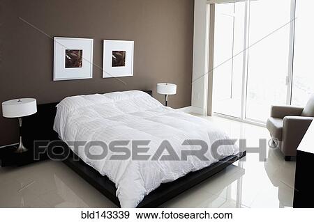 Stock Photo - Bed, wall art and windows in modern bedroom. Fotosearch
