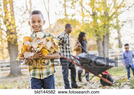 Stock Image - Boy holding pile of autumn leaves. Fotosearch