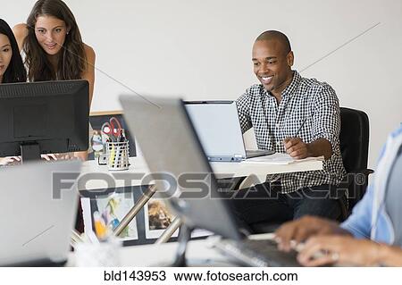 Stock Image - Business people working together on computers in office. Fotosearch