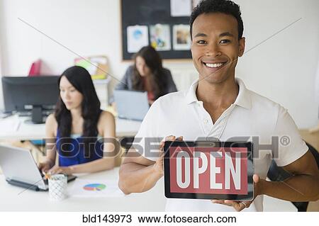 Stock Image - Businessman holding open sign on digital tablet in office. Fotosearch