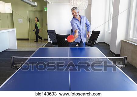 Stock Image - Businessman playing table tennis in office. Fotosearch