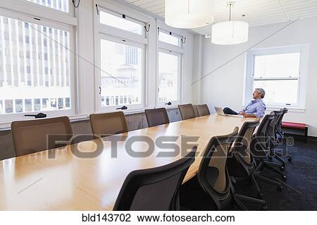 Stock Image - Businessman sitting at table in conference room. Fotosearch