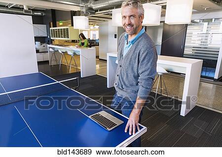 Businessman using laptop at table tennis table in office View Large Photo Image Stock Photo - Businessman using laptop at table tennis table in office. Fotosearch