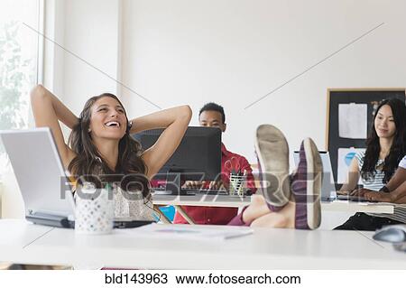 Stock Image - Businesswoman relaxing at desk in office. Fotosearch