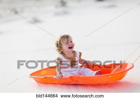 Picture - Caucasian boy sitting in sled on sand dune. Fotosearch