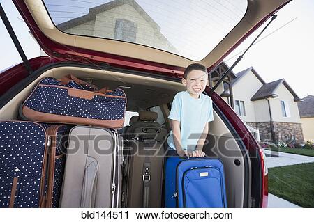 Stock Image - Caucasian boy smiling with suitcases in car. Fotosearch