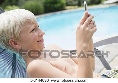 Stock Image - Caucasian boy using cell phone near swimming pool. Fotosearch