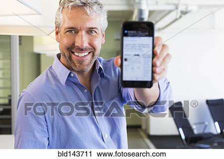 Stock Image - Caucasian businessman holding cell phone in office. Fotosearch