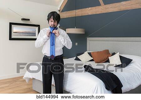 Caucasian businessman tying tie in bedroom View Large Photo Image Picture - Caucasian businessman tying tie in bedroom. Fotosearch