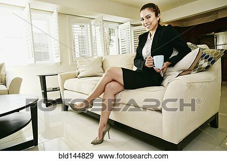 Stock Photo - Caucasian businesswoman drinking cup of coffee on sofa. Fotosearch