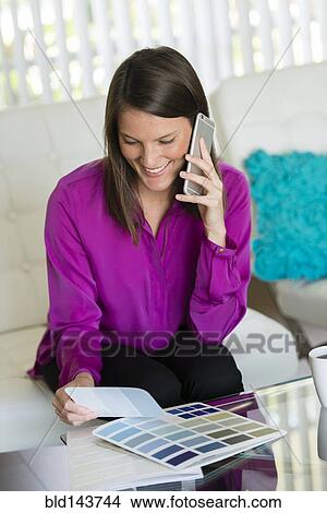 Picture - Caucasian businesswoman talking on cell phone and examining color swatches. Fotosearch