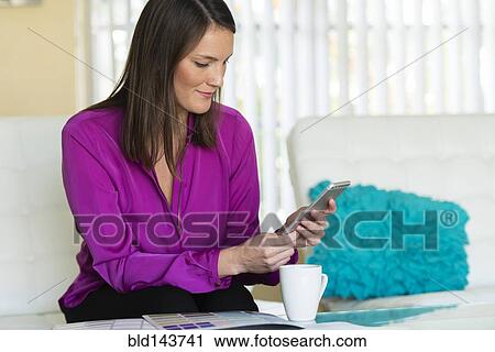 Stock Image - Caucasian businesswoman using cell phone on sofa. Fotosearch