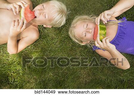 Stock Photo - Caucasian children eating watermelon on lawn. Fotosearch