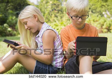 Stock Image - Caucasian children using digital tablets in backyard. Fotosearch