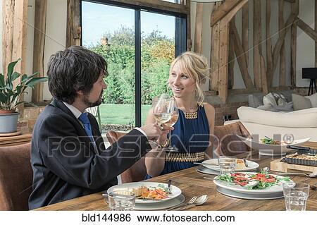 Stock Photograph - Caucasian couple toasting at dinner in dining room. Fotosearch