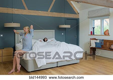 Stock Image - Caucasian couple waking in bedroom. Fotosearch
