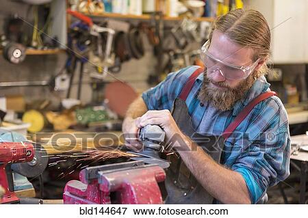 Stock Photo - Caucasian craftsman grinding in workshop. Fotosearch