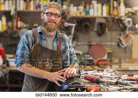 Stock Image - Caucasian craftsman smiling in workshop. Fotosearch
