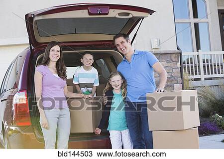 Stock Image - Caucasian family unpacking cardboard boxes from car. Fotosearch
