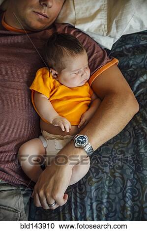Stock Image - Caucasian father and baby boy sleeping on bed. Fotosearch