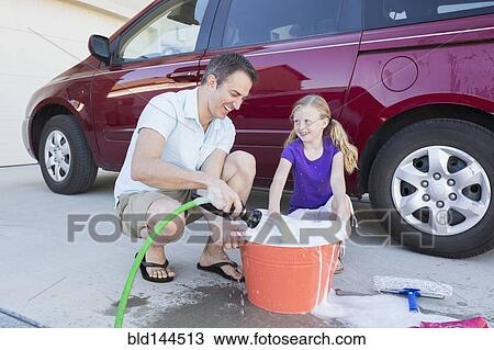 Stock Image - Caucasian father and daughter washing car in driveway. Fotosearch