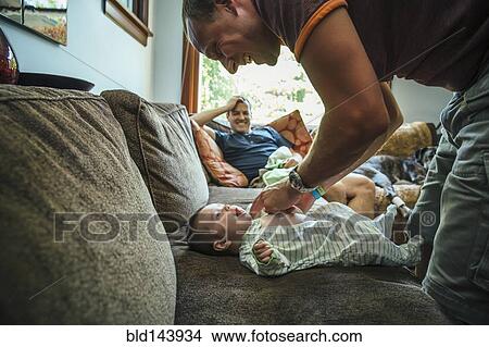 Picture - Caucasian father dressing baby boy on sofa. Fotosearch