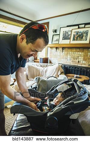Stock Photo - Caucasian father fastening baby boy in car seat. Fotosearch