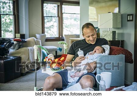 Stock Photo - Caucasian father feeding baby boy in living room. Fotosearch