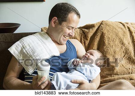 Stock Image - Caucasian father holding baby boy in living room. Fotosearch