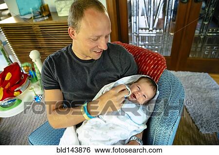 Stock Photograph - Caucasian father holding baby boy in armchair. Fotosearch
