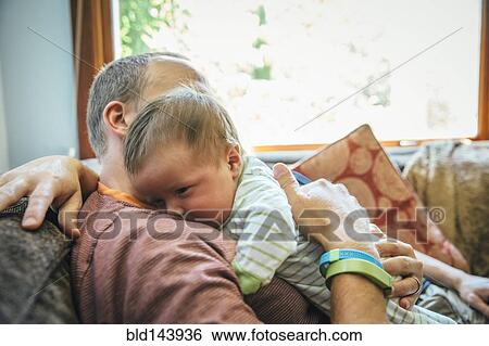 Stock Photograph - Caucasian father holding baby boy on sofa. Fotosearch