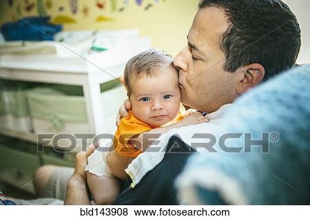 Stock Photo - Caucasian father kissing baby boy in nursery. Fotosearch