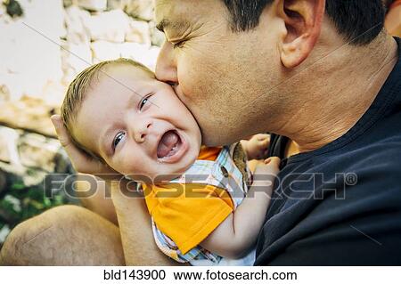 Stock Image - Caucasian father kissing baby boy outdoors. Fotosearch