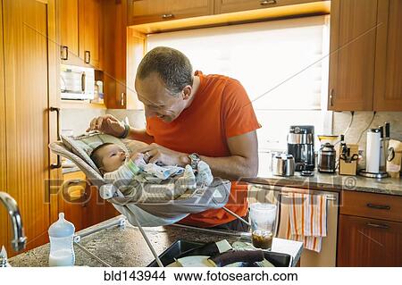 Picture - Caucasian father playing with baby boy in kitchen. Fotosearch