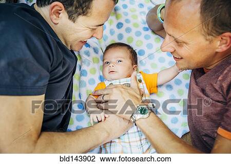 Stock Image - Caucasian gay couple cuddling baby boy. Fotosearch
