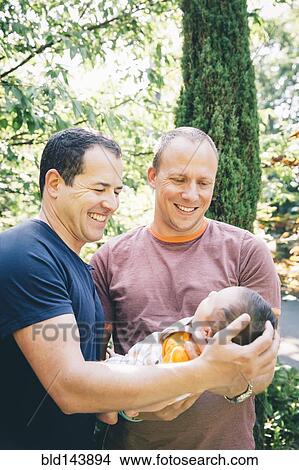 Picture - Caucasian gay couple holding baby boy outdoors. Fotosearch
