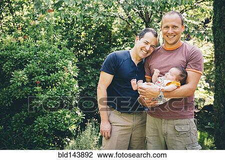 Stock Image - Caucasian gay couple holding baby boy outdoors. Fotosearch