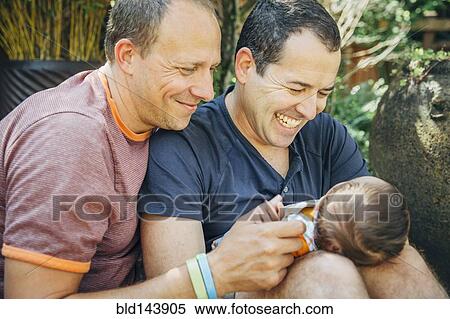 Stock Photography - Caucasian gay couple holding baby boy outdoors. Fotosearch