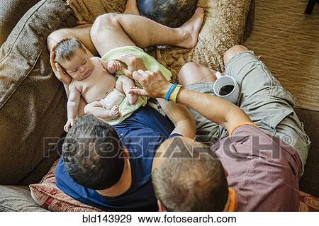 Caucasian gay couple holding sleeping baby boy on sofa View Large Photo Image Stock Photo - Caucasian gay couple holding sleeping baby boy on sofa. Fotosearch