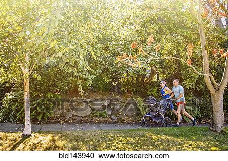 Stock Image - Caucasian gay couple jogging with stroller on sidewalk. Fotosearch