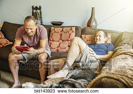 Stock Image - Caucasian gay couple relaxing in living room. Fotosearch