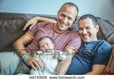 Stock Photography - Caucasian gay couple smiling with baby boy on sofa. Fotosearch
