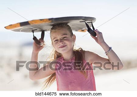 Stock Photography - Caucasian girl carrying sled on sand dune. Fotosearch