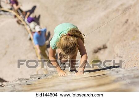 Picture - Caucasian girl climbing wooden ladder on hillside. Fotosearch