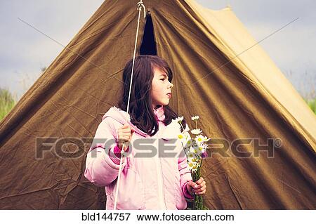 Stock Photo - Caucasian girl holding wildflowers near camp tent. Fotosearch