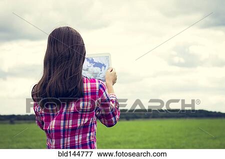 Stock Photo - Caucasian girl taking photograph with tablet computer in grassy field. Fotosearch
